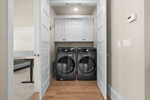 Washroom featuring washing machine and clothes dryer, visible vents, cabinet space, and light wood-type flooring