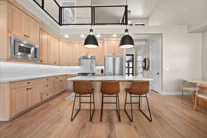 Kitchen with under cabinet range hood, light brown cabinets, light wood-type flooring, and appliances with stainless steel finishes