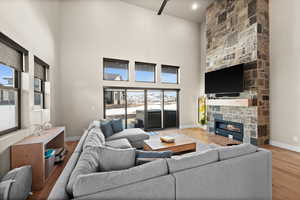 Living room with baseboards, a stone fireplace, wood finished floors, and a towering ceiling