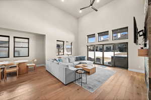 Living room featuring light wood-type flooring, a ceiling fan, recessed lighting, a high ceiling, and baseboards