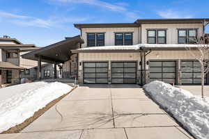 View of front facade with board and batten siding, an attached garage, stone siding, and driveway