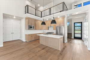 Kitchen featuring a center island with sink, appliances with stainless steel finishes, light hardwood / wood-style floors, a towering ceiling, and sink