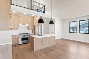 Kitchen with sink, pendant lighting, an island with sink, light brown cabinetry, and premium appliances