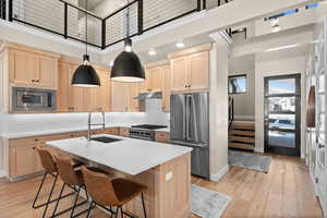 Kitchen featuring under cabinet range hood, light brown cabinets, high quality appliances, and a towering ceiling