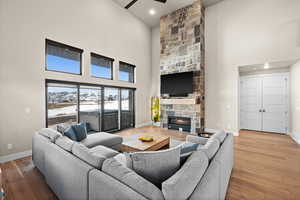 Living room featuring baseboards, a high ceiling, ceiling fan, a stone fireplace, and light wood-type flooring