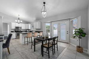 Dining area with sink, light tile patterned floors, an inviting chandelier, and vaulted ceiling