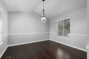 Spare room with lofted ceiling, dark hardwood / wood-style flooring, and a chandelier