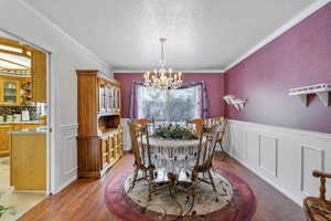 Dining room featuring a textured ceiling, crown molding, a chandelier, and hardwood / wood-style floors