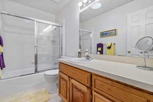 Full bathroom with toilet, bath / shower combo with glass door, and vanity