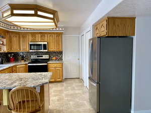 Kitchen with appliances with stainless steel finishes, a textured ceiling, light stone countertops, backsplash, and kitchen peninsula