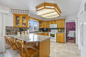 Kitchen with white appliances, kitchen peninsula, a kitchen bar, decorative backsplash, and sink