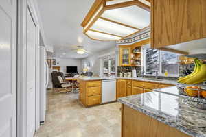 Kitchen featuring light stone countertops, kitchen peninsula, white dishwasher, ceiling fan, and sink