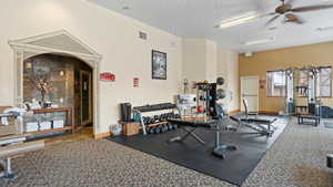 Gym featuring a textured ceiling, ceiling fan, and carpet floors