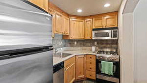 Kitchen featuring sink, stainless steel appliances, backsplash, and light stone countertops