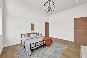 Bedroom featuring an inviting chandelier, high vaulted ceiling, and wood-type flooring