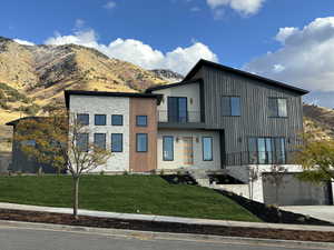 Modern home with a balcony, a front lawn, and a mountain view