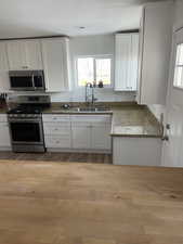 Kitchen with white cabinets, stainless steel appliances, a textured ceiling, sink, and stone countertops