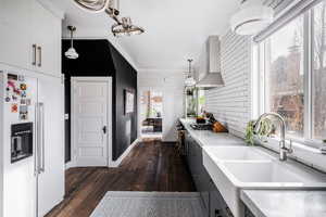 Kitchen with sink, white cabinetry, wall chimney range hood, pendant lighting, and high end fridge