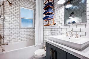 Full bathroom featuring shower / bath combination with curtain, toilet, vanity, tile walls, and decorative backsplash