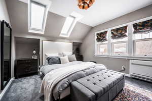 Carpeted bedroom featuring vaulted ceiling with skylight and heating unit