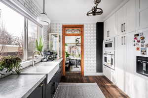 Kitchen featuring dark wood-type flooring, decorative light fixtures, brick wall, refrigerator with ice dispenser, and white cabinetry