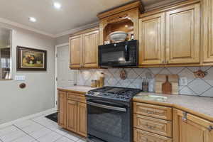 Kitchen featuring range with gas stovetop, crown molding, light tile patterned floors, and decorative backsplash