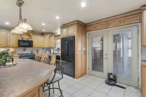 Kitchen with black appliances, hanging light fixtures, light tile patterned floors, french doors, and sink