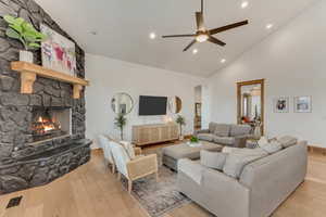 Living room with ceiling fan, a stone fireplace, high vaulted ceiling, and light wood-type flooring