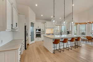 Kitchen featuring white cabinetry, a kitchen island with sink, pendant lighting, stainless steel appliances, and light hardwood / wood-style floors