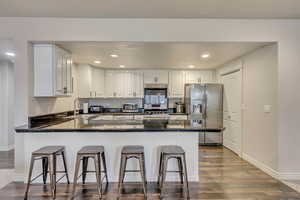 Kitchen featuring dark wood-type flooring, a breakfast bar, white cabinetry, appliances with stainless steel finishes, and kitchen peninsula