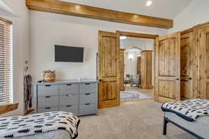 Bedroom with beamed ceiling, light carpet, and decorative columns