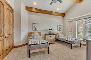 Carpeted bedroom featuring ceiling fan and vaulted ceiling with beams