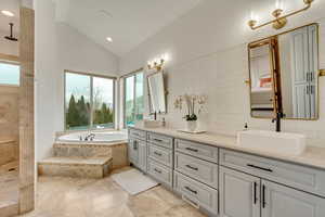 Bathroom featuring tiled tub, vaulted ceiling, backsplash, and vanity