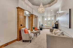 Carpeted living room with decorative columns, a chandelier, and a tray ceiling