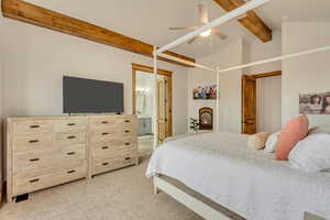 Carpeted bedroom featuring lofted ceiling with beams, ceiling fan, and ensuite bath