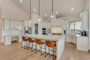 Kitchen with light hardwood / wood-style flooring, appliances with stainless steel finishes, a kitchen island with sink, white cabinetry, and decorative light fixtures