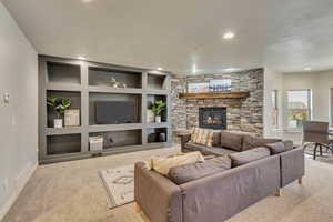 Living room with a stone fireplace, light colored carpet, and built in features