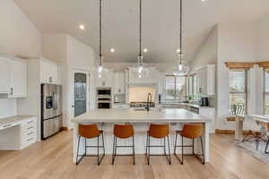 Kitchen featuring a kitchen island with sink, hanging light fixtures, high vaulted ceiling, stainless steel appliances, and white cabinets