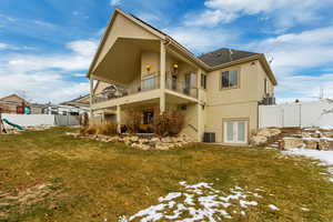 Snow covered back of property with cooling unit, a yard, french doors, and a balcony