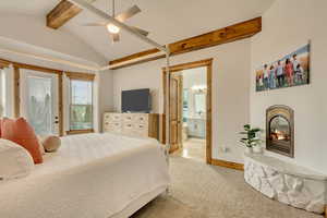 Bedroom with lofted ceiling with beams, ceiling fan, light colored carpet, and ensuite bath