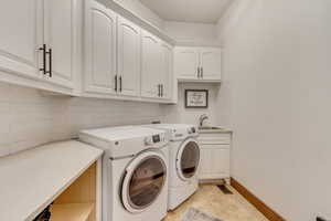 Laundry room with cabinets, sink, light tile patterned floors, and washing machine and clothes dryer