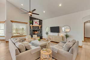 Living room featuring ceiling fan, a stone fireplace, high vaulted ceiling, and light hardwood / wood-style floors