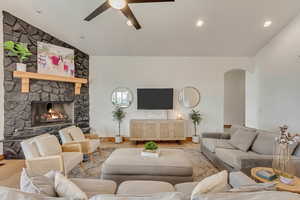 Living room with ceiling fan, a stone fireplace, vaulted ceiling, and light wood-type flooring