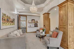 Living room featuring a tray ceiling, ceiling fan with notable chandelier, and light carpet