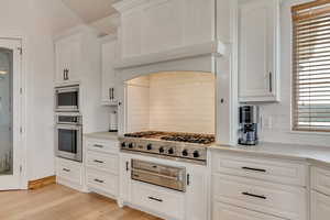 Kitchen with decorative backsplash, stainless steel appliances, light hardwood / wood-style flooring, and white cabinets