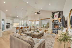 Living room with a stone fireplace, light hardwood / wood-style flooring, high vaulted ceiling, and ceiling fan