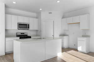 Kitchen featuring light wood finished floors, a center island with sink, white cabinets, appliances with stainless steel finishes, and a sink