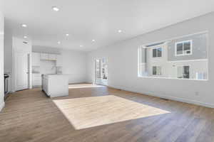 Kitchen featuring recessed lighting, a sink, white cabinetry, light wood finished floors, and a center island with sink