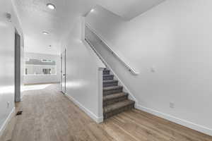 Stairway with baseboards, a textured ceiling, visible vents, and wood finished floors