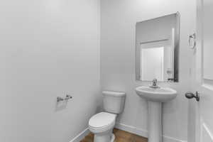 Half bathroom featuring toilet, baseboards, and wood finished floors